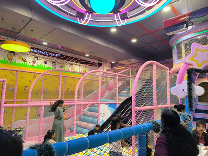 Children play in a colorful indoor playground with slides and ball pits, supervised by adults.