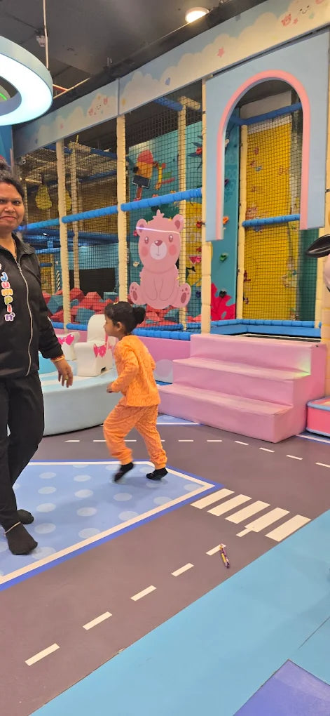 A woman watches a young child run in a colorful indoor play area.
