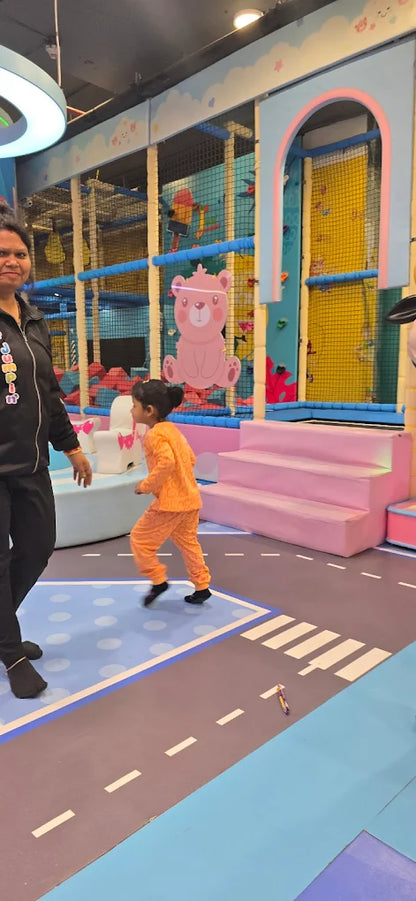 A woman watches a young child run in a colorful indoor play area.