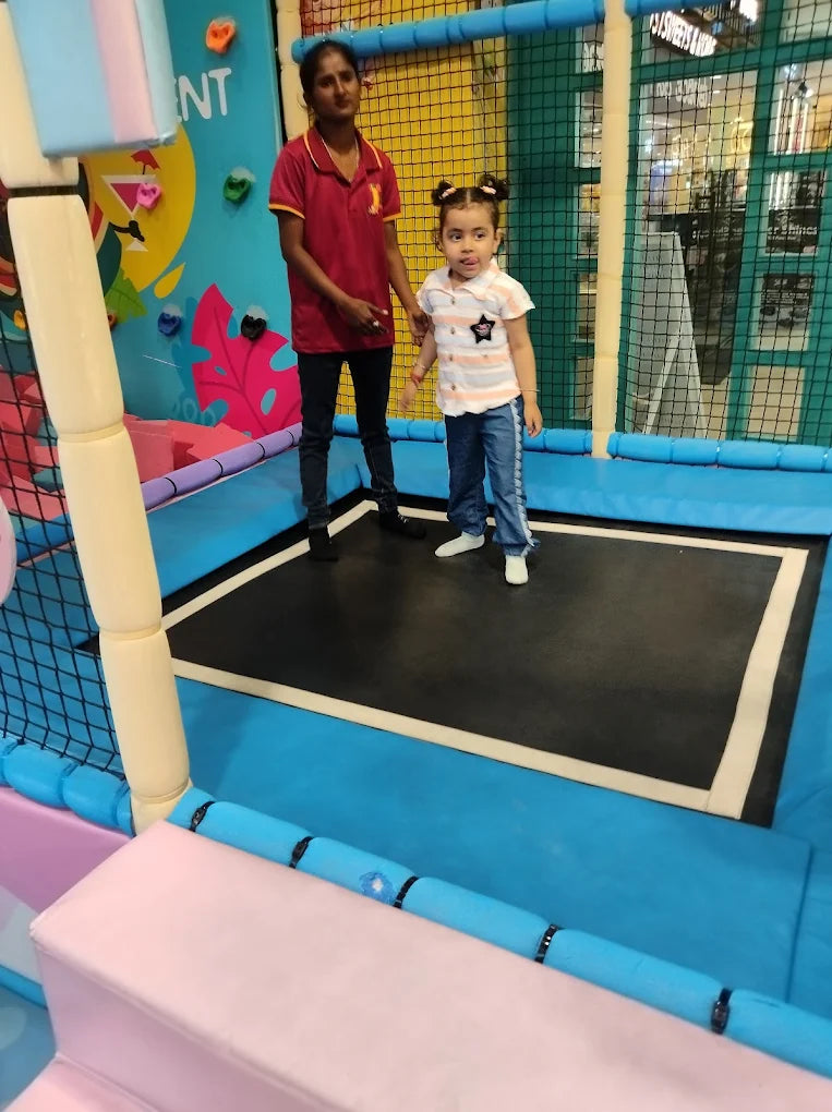 A woman supervises a young child on a trampoline in a colorful indoor play area.