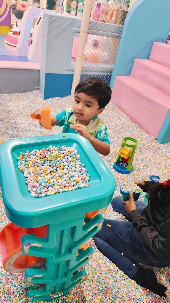 A young boy plays with colorful balls in a ball pit, with another child in the foreground.