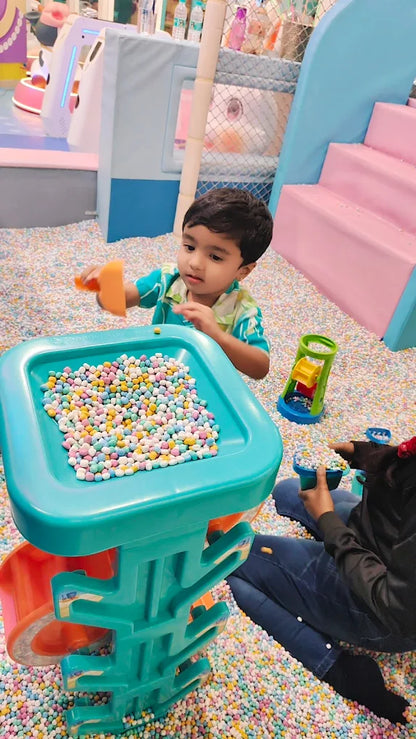 A young boy plays with colorful balls in a ball pit, with another child in the foreground.