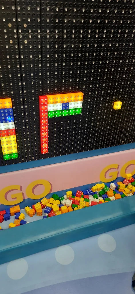 A wall of lights displays an Indian flag made of colorful blocks, with a bin of toy blocks below.