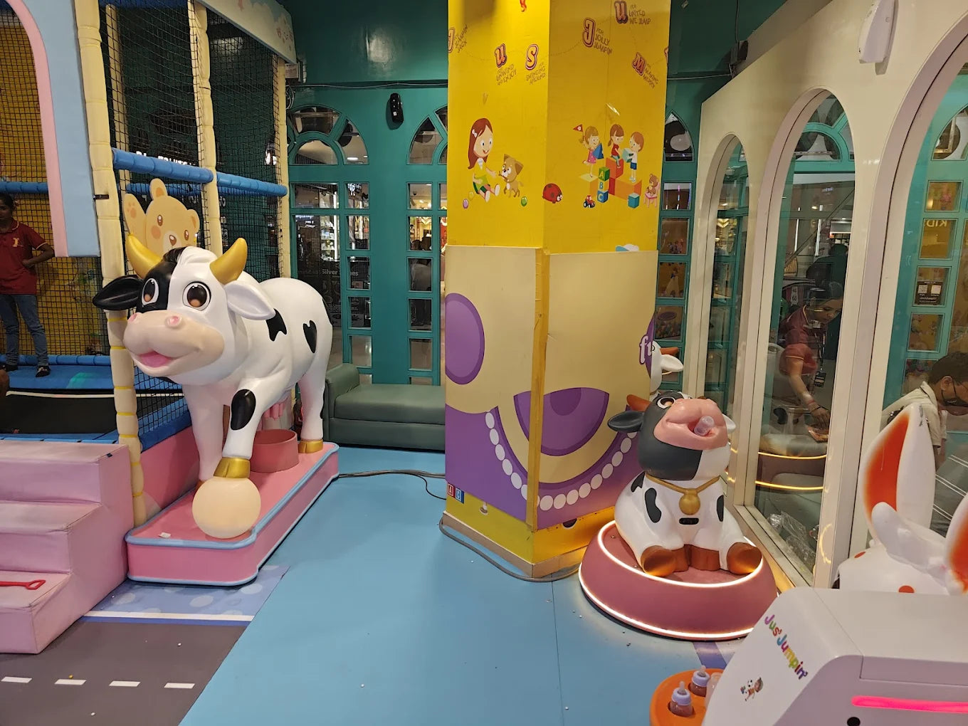 A playful indoor playground with large cow decorations and children's play structures.