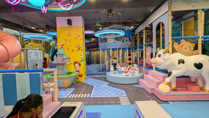 A colorful indoor playground with children playing, featuring a large cow statue and a carousel.