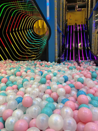 A ball pit filled with pink, blue, and white balls, with a colorful tunnel and slide in the background.