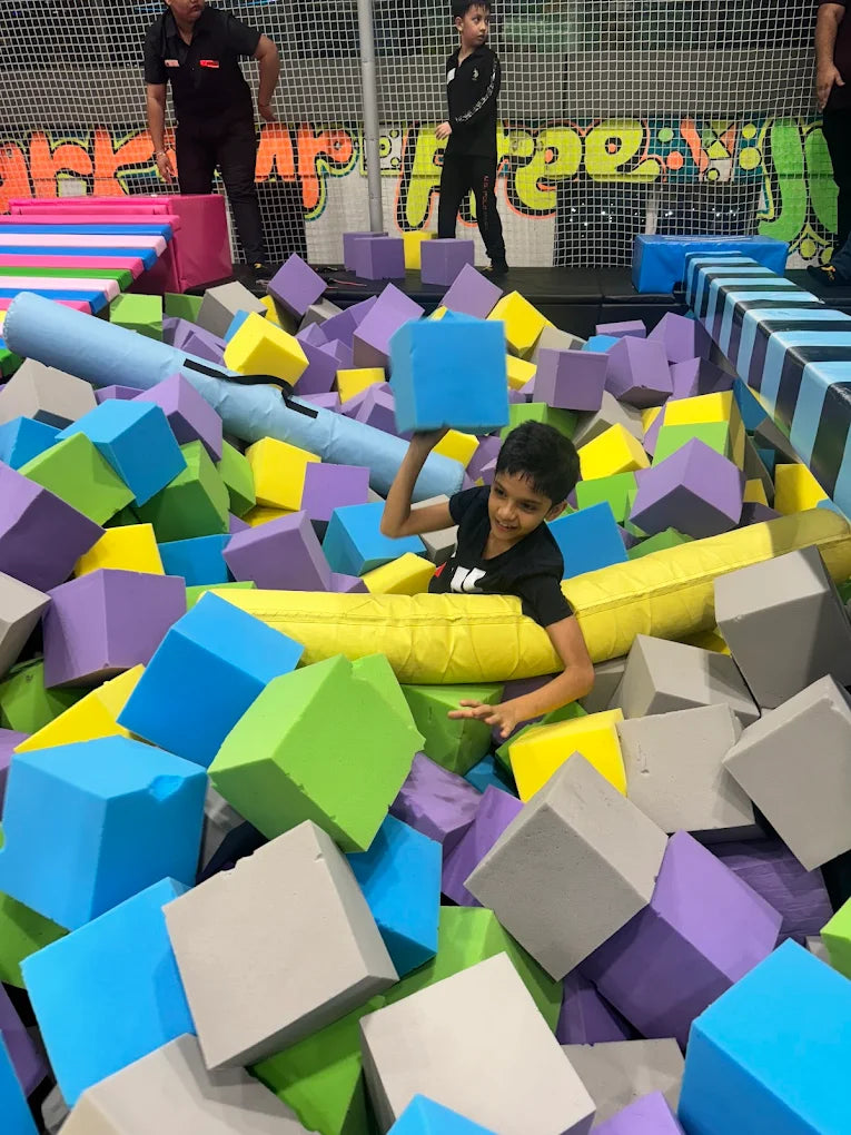 Child playing in a colorful foam pit with various geometric shapes.