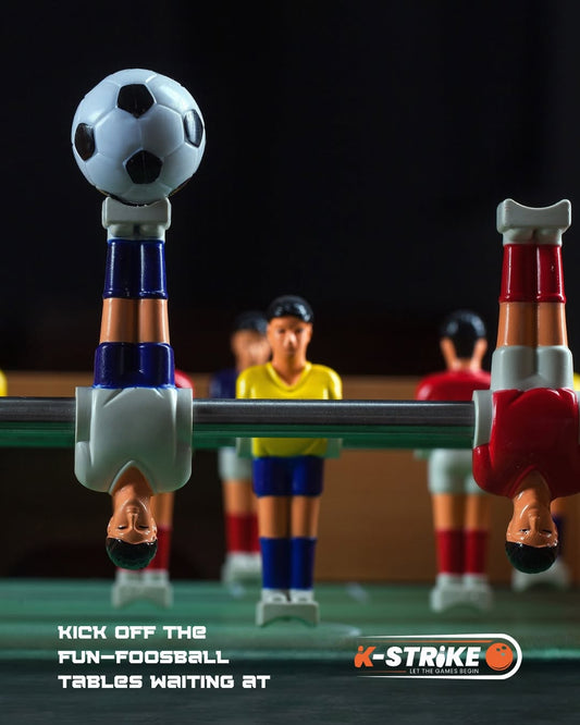 Foosball players on a table, with a soccer ball on top.
