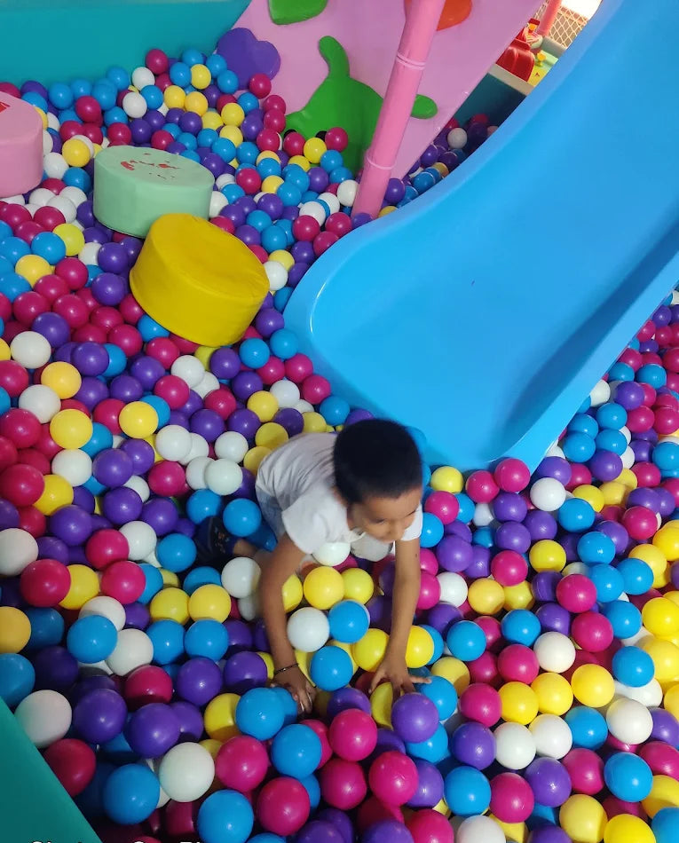 A young child plays in a ball pit with a blue slide.