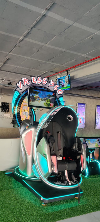 A futuristic VR egg chair with a screen displays a game, set up on artificial grass.