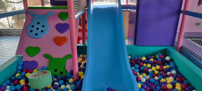 A colorful indoor playground with a blue slide and ball pit, featuring soft play shapes for young children.