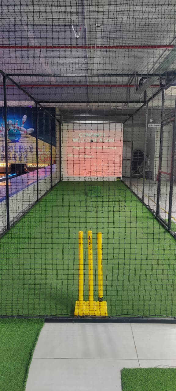 A cricket net with wickets and a screen displaying scores.
