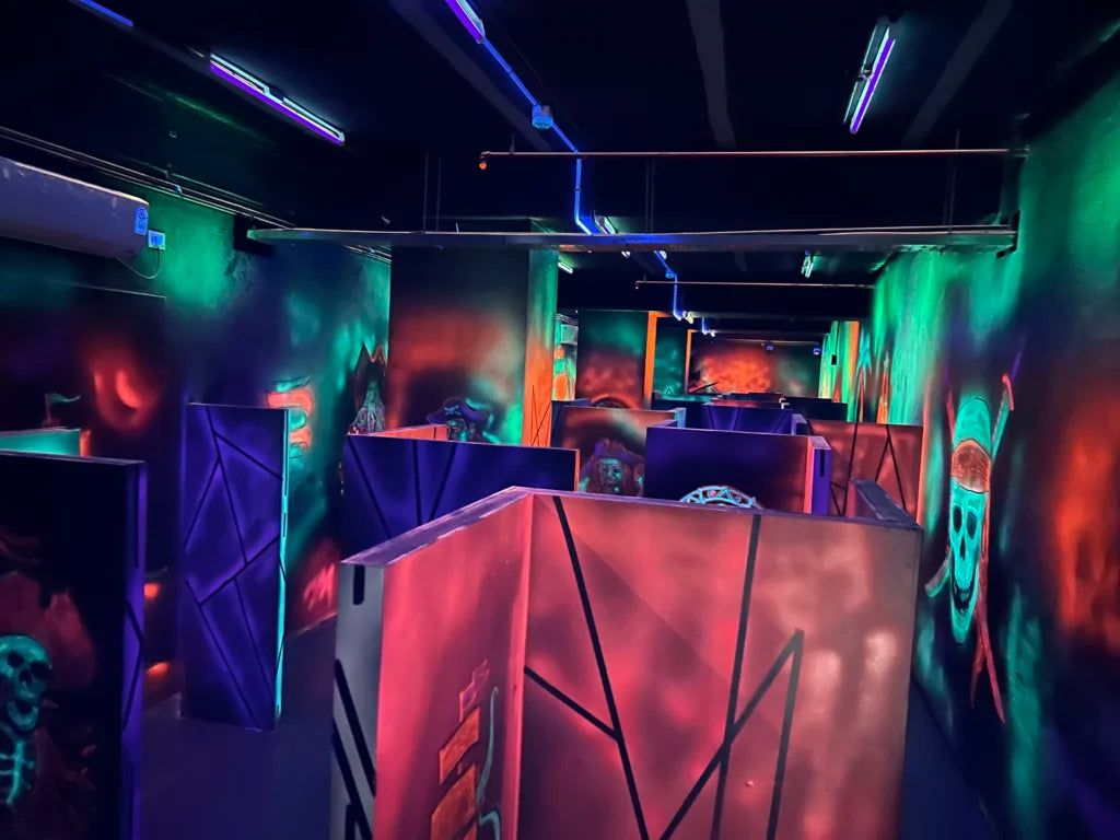 A neon-lit laser tag arena with pirate-themed murals and maze-like walls.