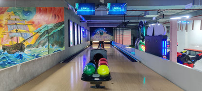 Bowling alley with colorful balls on a rack and a mural of a ship.