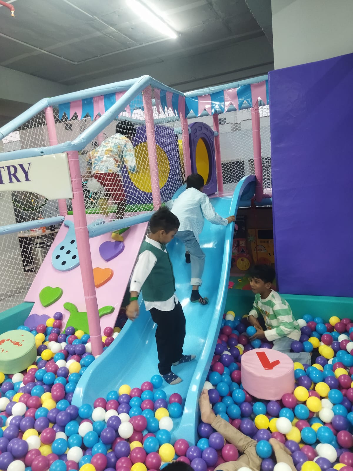 Children play on a colorful indoor playground with a slide and ball pit.