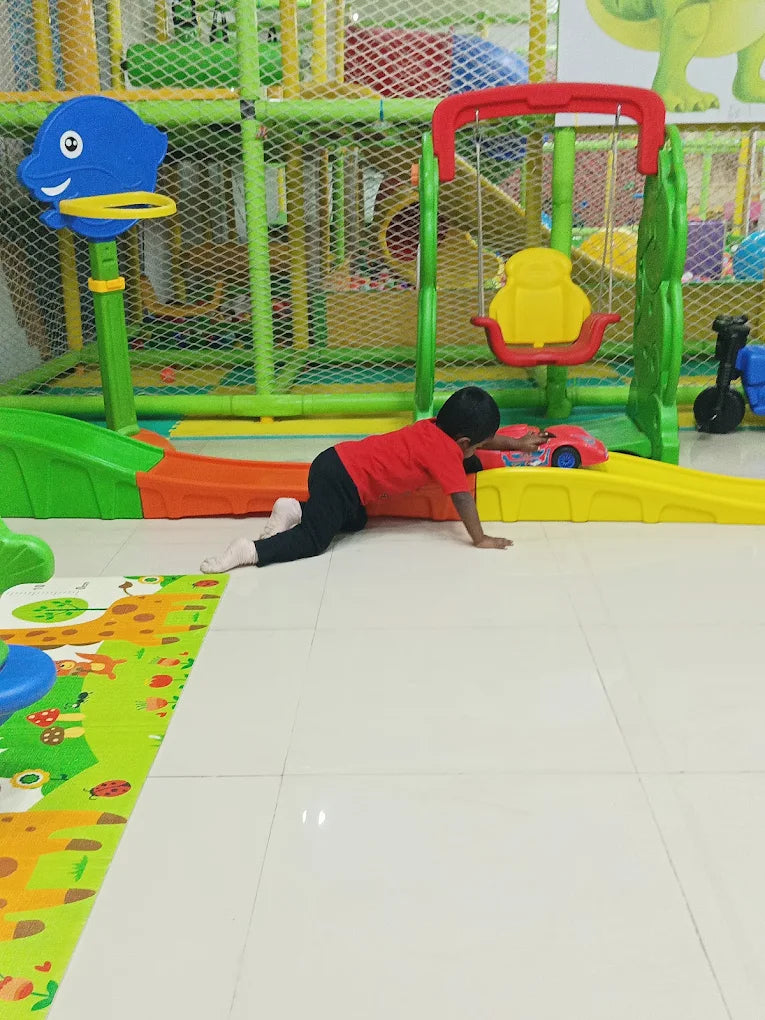 A young child crawls on a play mat in a colorful indoor playground.