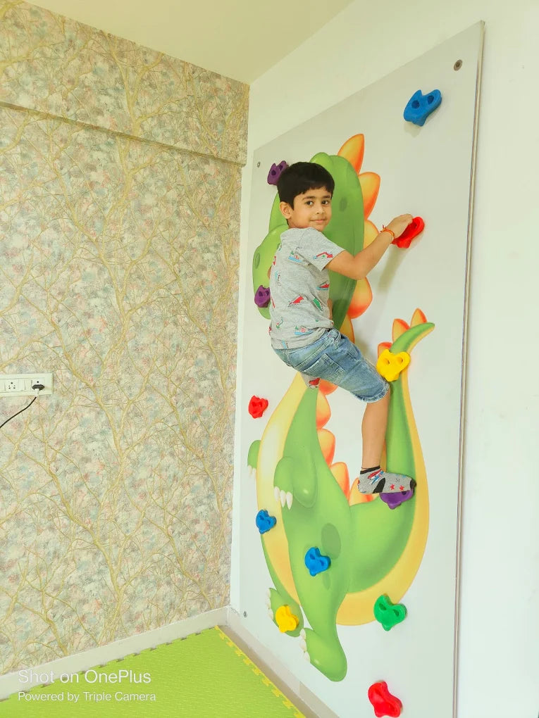 A young boy climbs a colorful dragon-themed wall with handholds.
