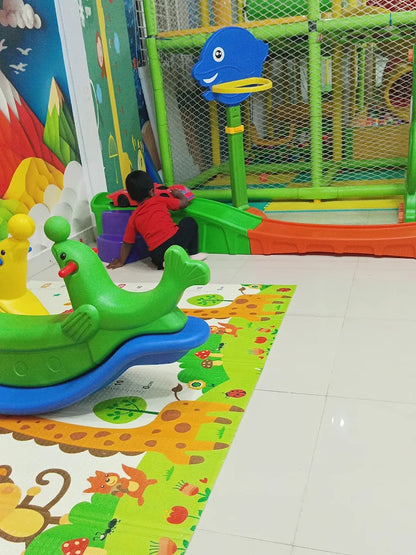 A young child plays with a toy car on a colorful play mat in a brightly decorated indoor play area.