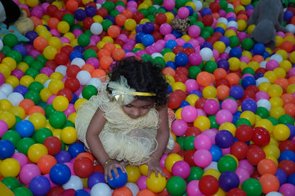 A young child in a yellow dress plays in a ball pit filled with colorful balls.