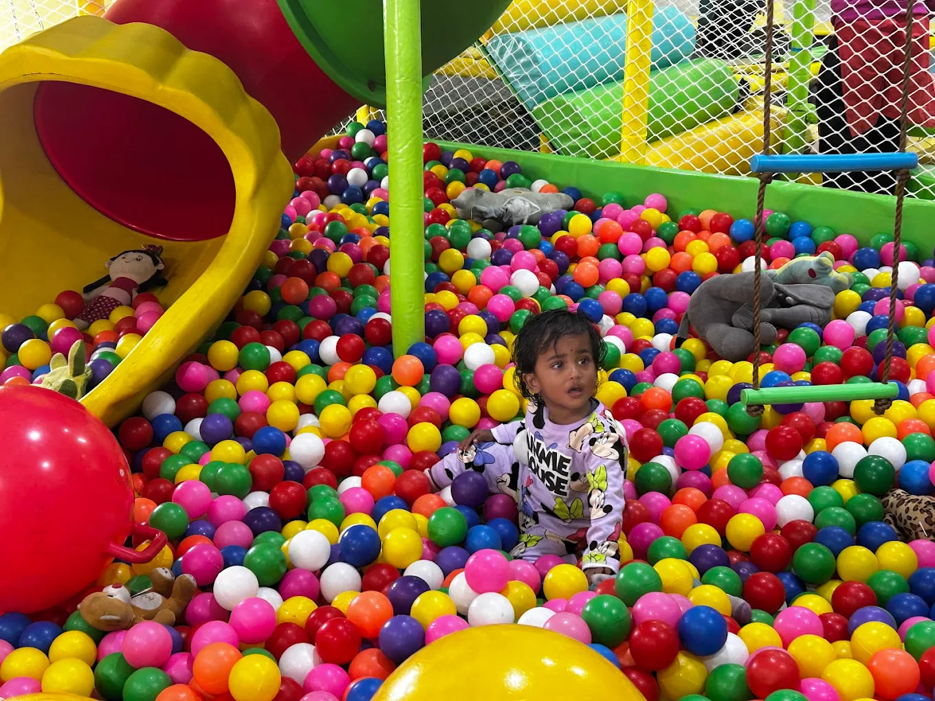 A young child sits in a ball pit with a stuffed elephant.