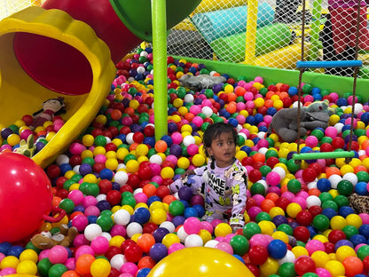 A young child sits in a ball pit with a stuffed elephant.