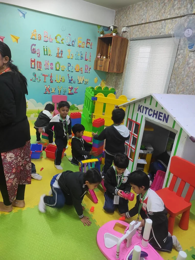 Young children play with building blocks and a play kitchen in a brightly decorated classroom.