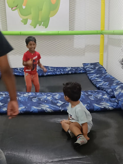 Two young boys are playing on a trampoline in a brightly decorated indoor play area.