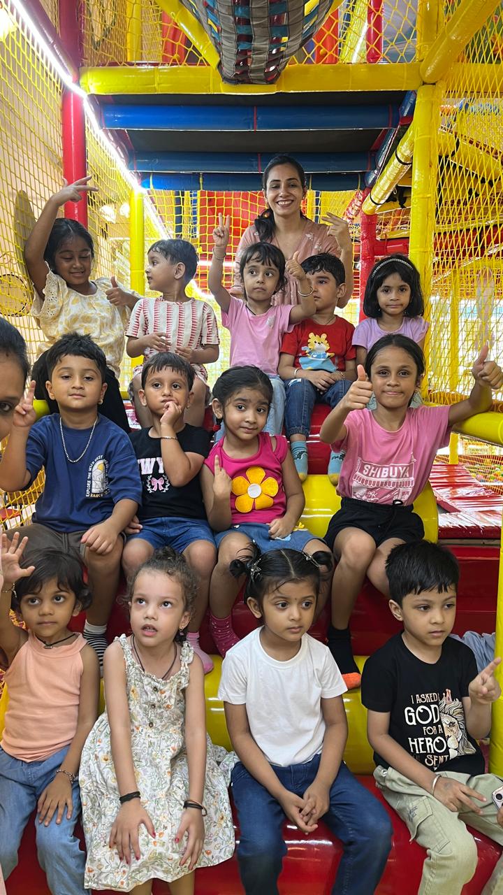 A group of children and one adult pose for a photo in a colorful indoor playground.