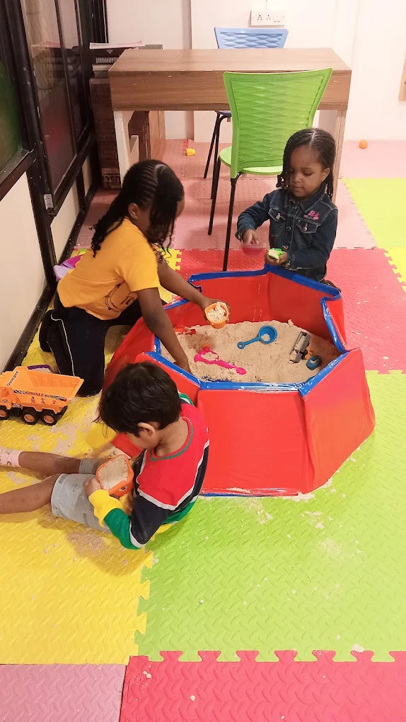 Children play in a sandbox with toys.