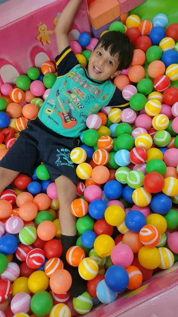A young boy smiles while playing in a ball pit filled with colorful balls.