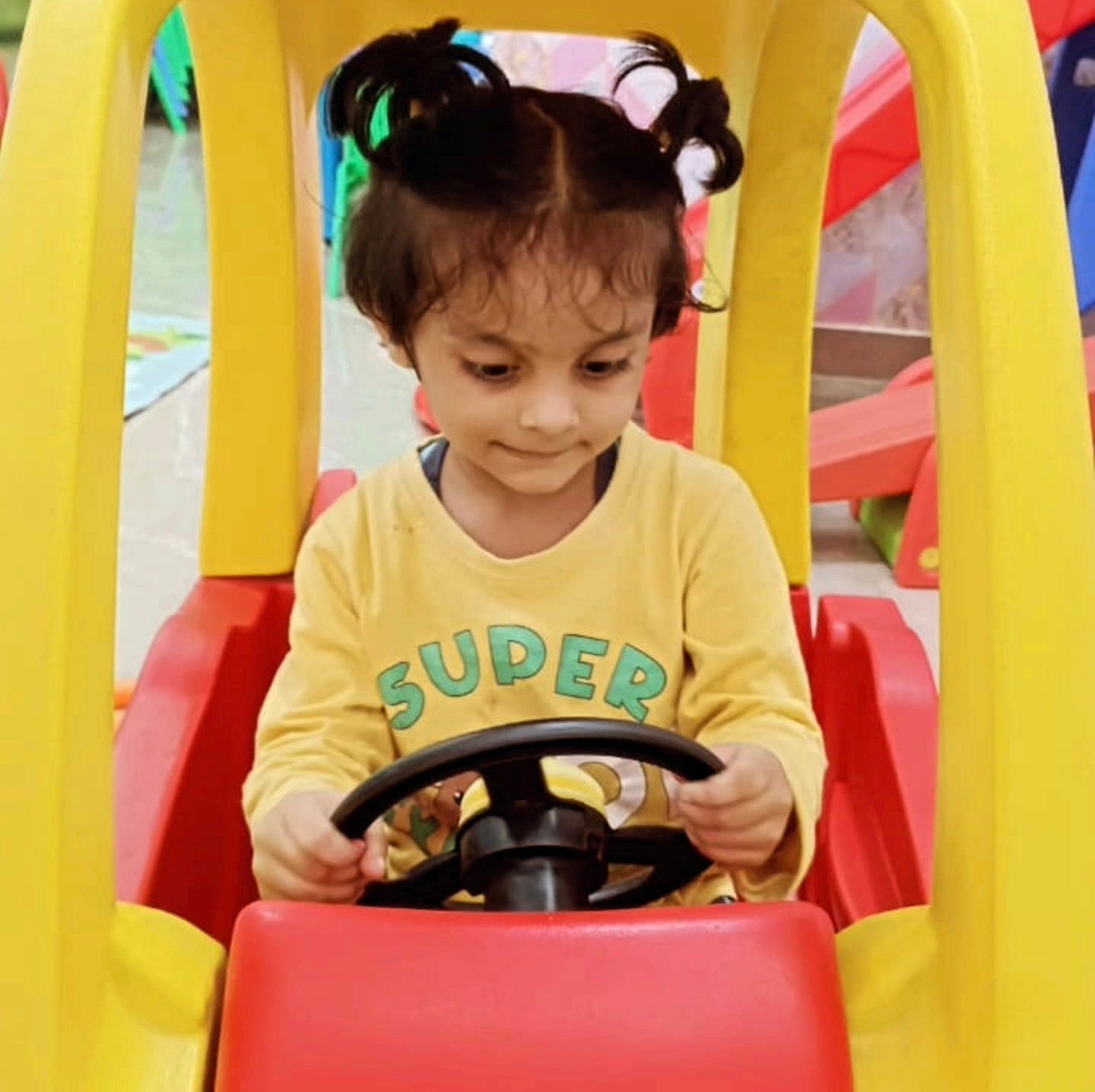 Child playing with a toy car, wearing a yellow shirt with 'SUPER' text.