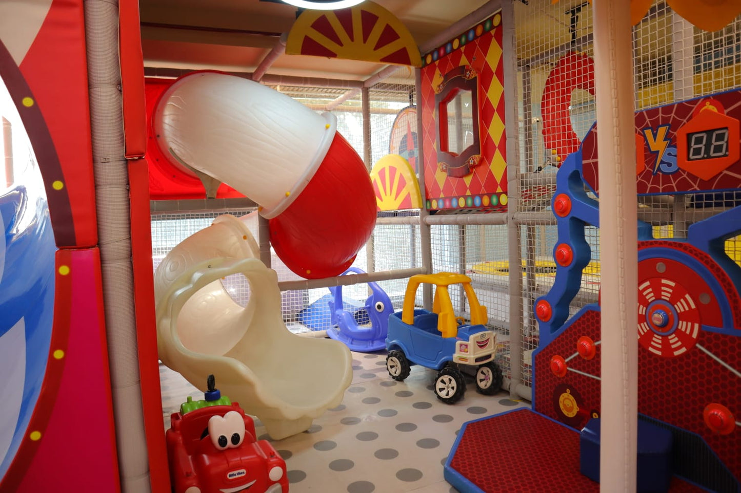 A colorful indoor playground with slides, toy cars, and a game for young children.