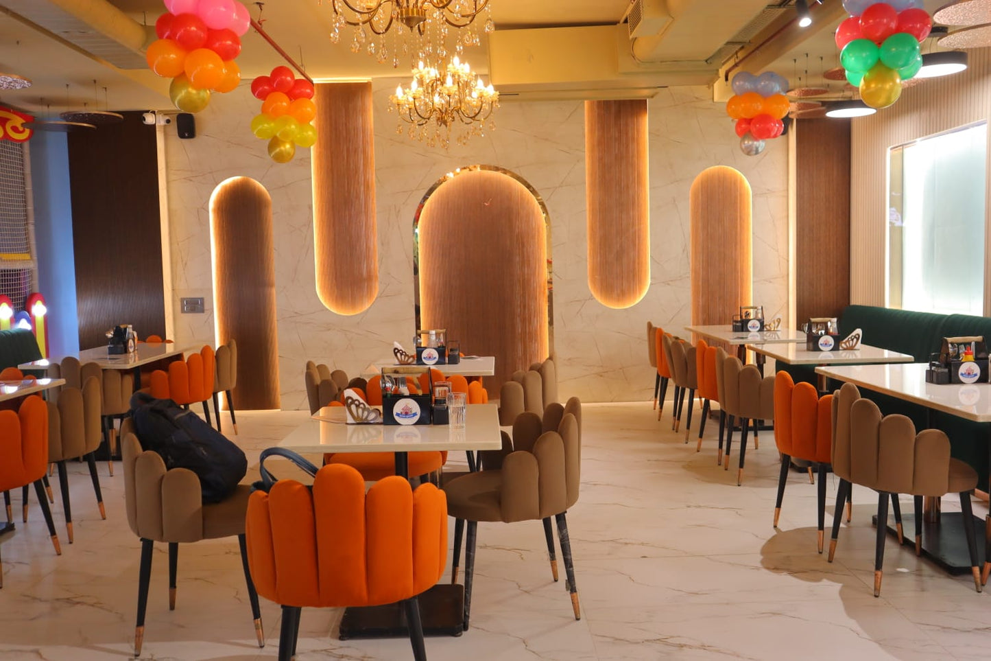 A restaurant dining area with marble floors, orange and brown chairs, and decorative balloons.