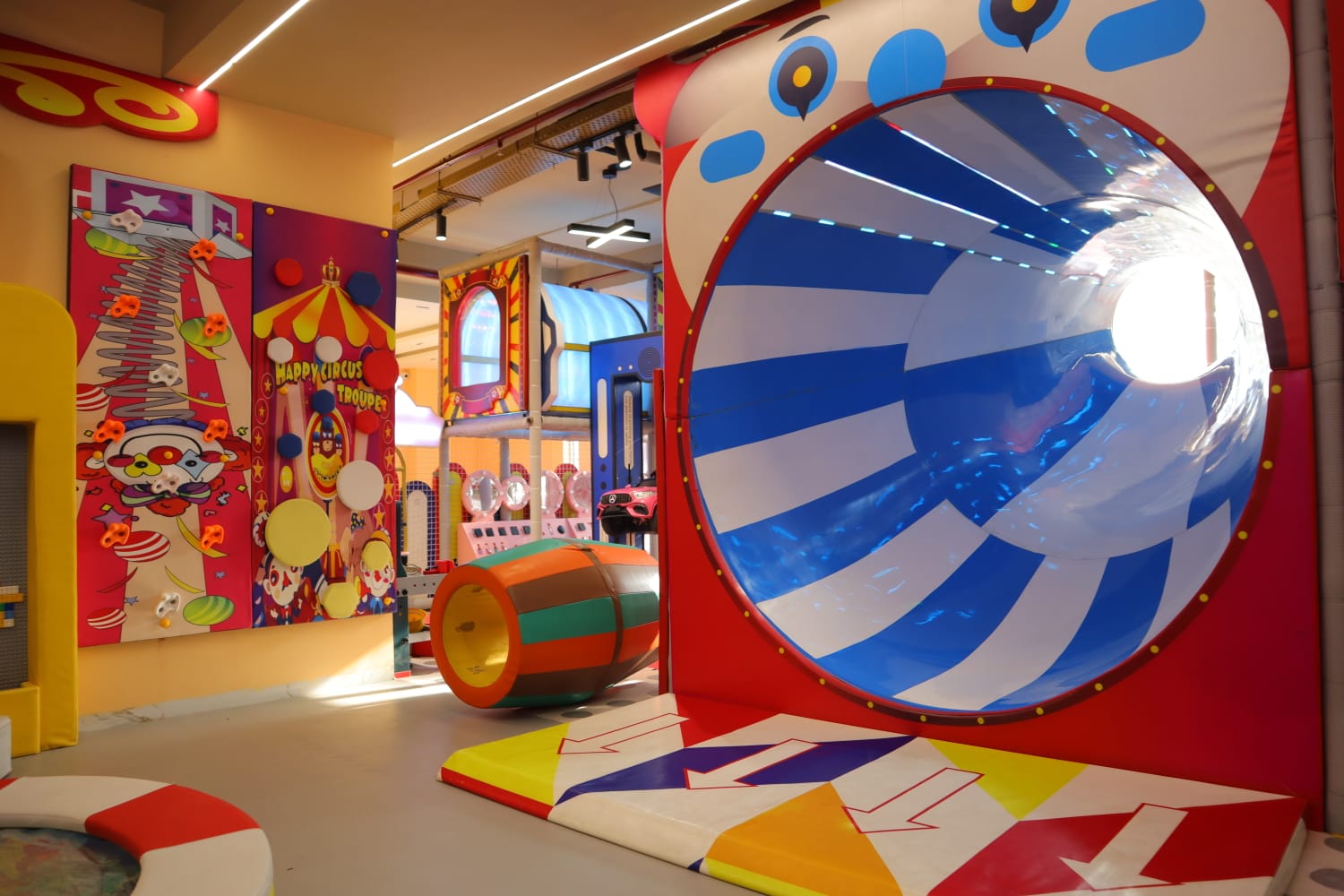 A colorful indoor playground with a large tube slide and circus-themed decorations. Children can play and explore the fun environment.
