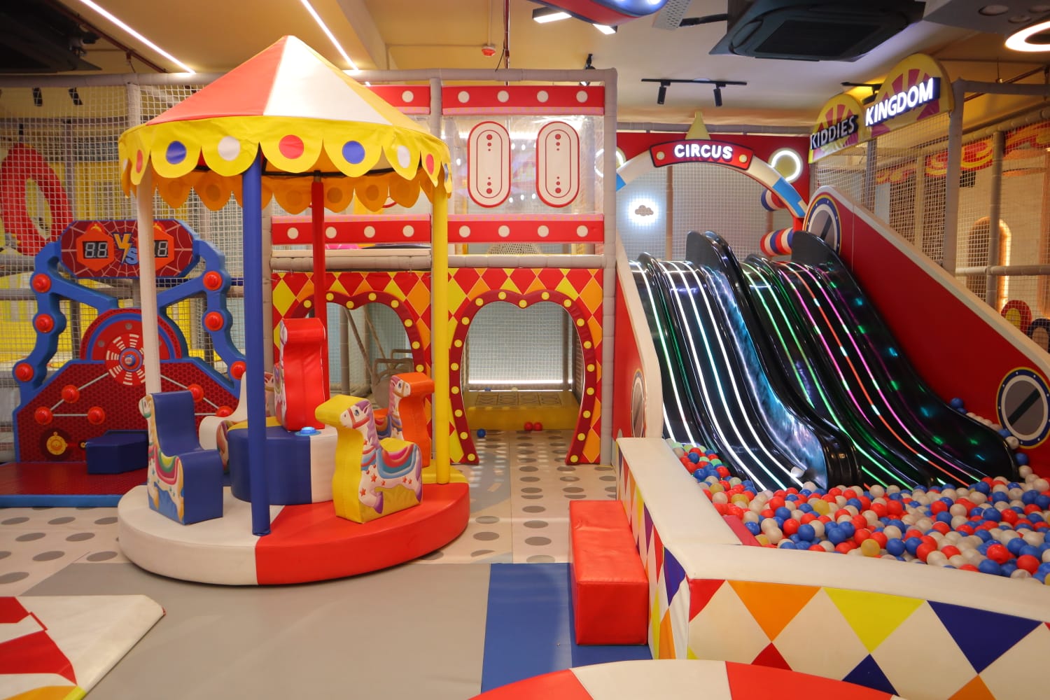 A colorful indoor playground with slides, a carousel, and a ball pit for young children.