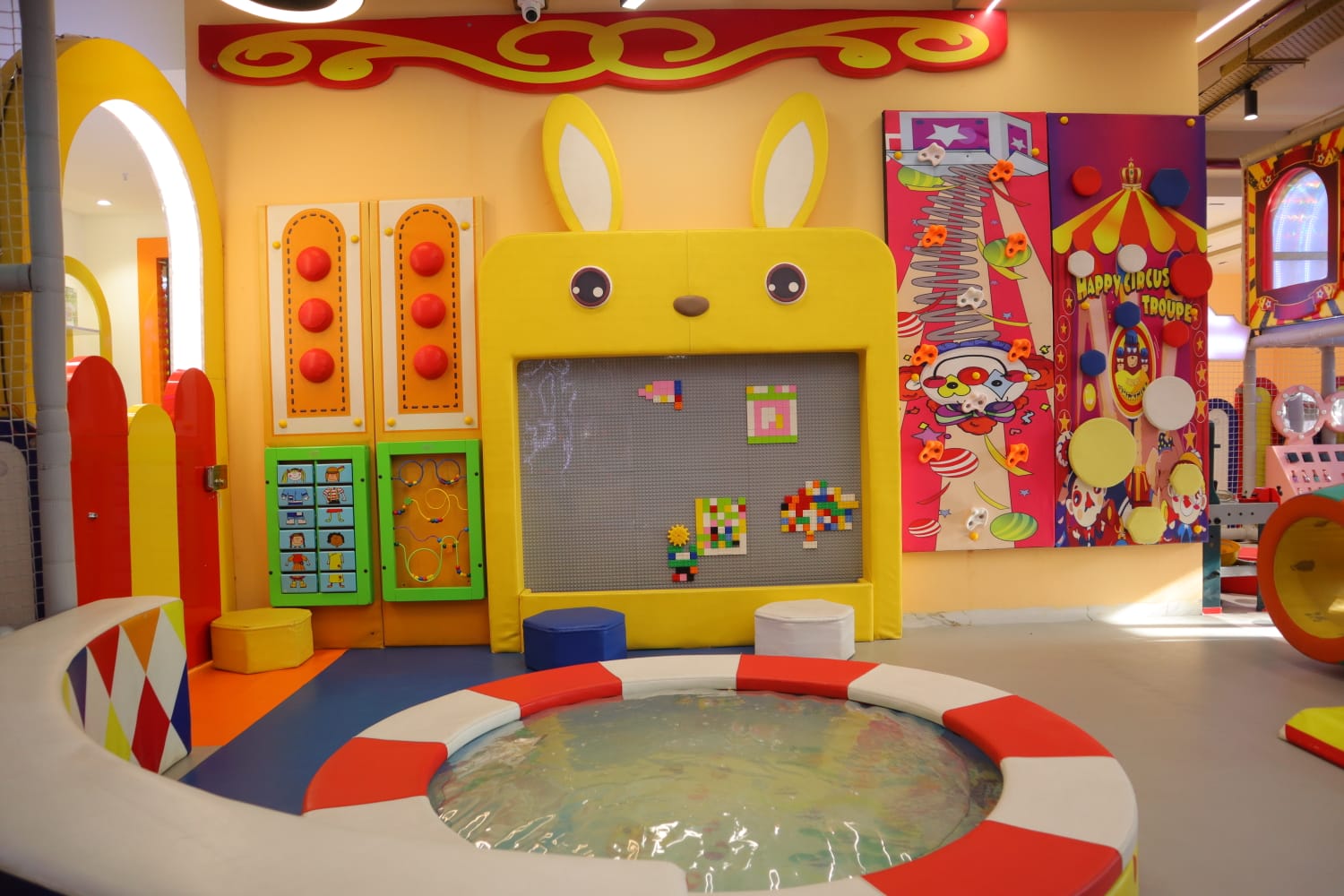 A colorful indoor playground with a shallow pool and interactive games for young children.