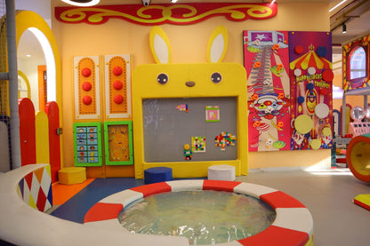 A colorful indoor playground with a shallow pool and interactive games for young children.