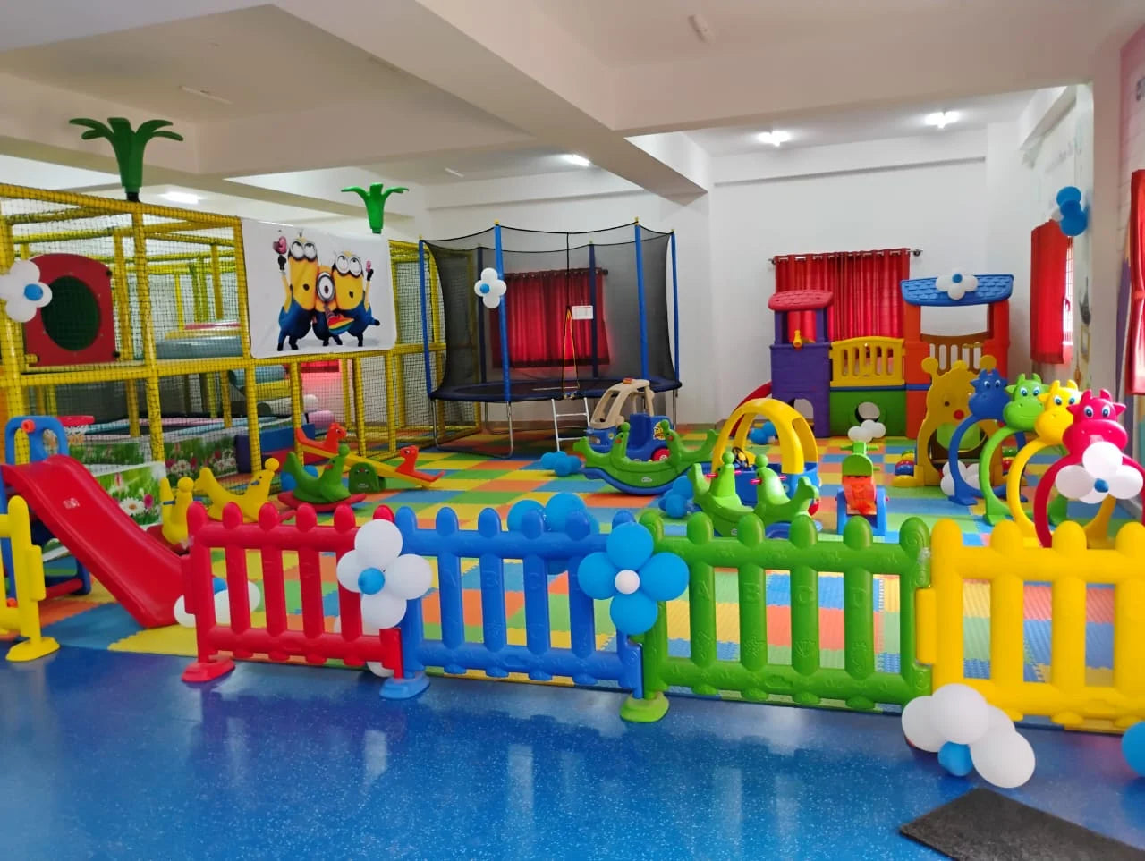A colorful indoor playground with soft play structures, slides, and a trampoline for young children.