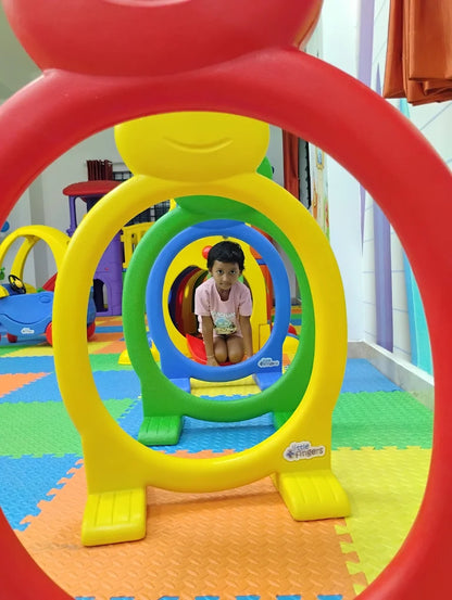 A young child sits inside a colorful, multi-ringed play structure.