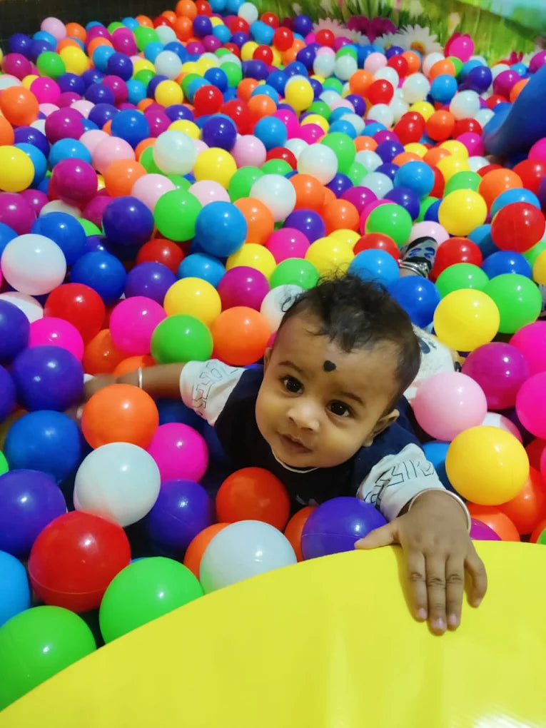 A baby lies in a ball pit, surrounded by colorful plastic balls.