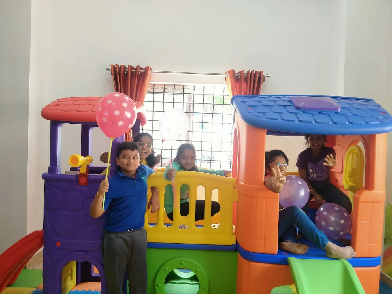Children play in a colorful indoor playhouse with balloons.