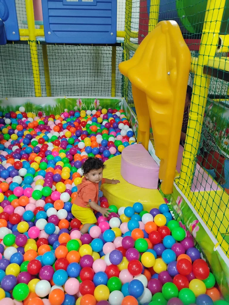 A toddler plays in a ball pit at an indoor playground.