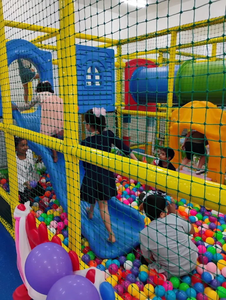Children play in a colorful indoor playground with ball pits and slides.