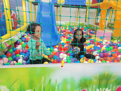 Two young children play in a colorful ball pit with a blue slide in the background.