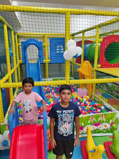 Two young boys stand in a colorful indoor playground filled with ball pits and play structures.