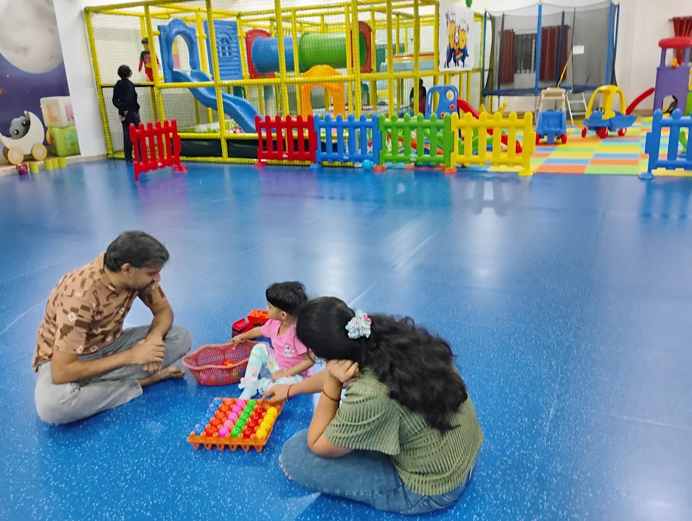 A family plays with toys on the floor of a colorful indoor playground.