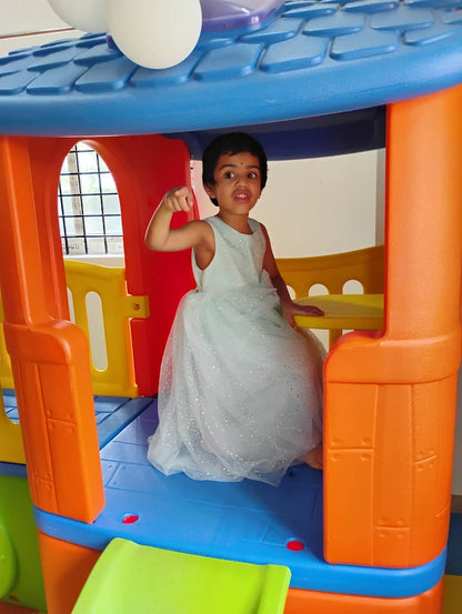 A young girl in a sparkly dress poses inside a colorful playhouse.