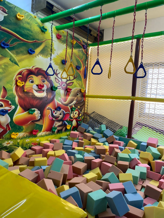 A colorful indoor playground with a foam pit, climbing wall, and jungle-themed mural.