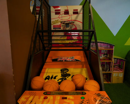 An arcade basketball game with orange balls and a dollhouse in the background.