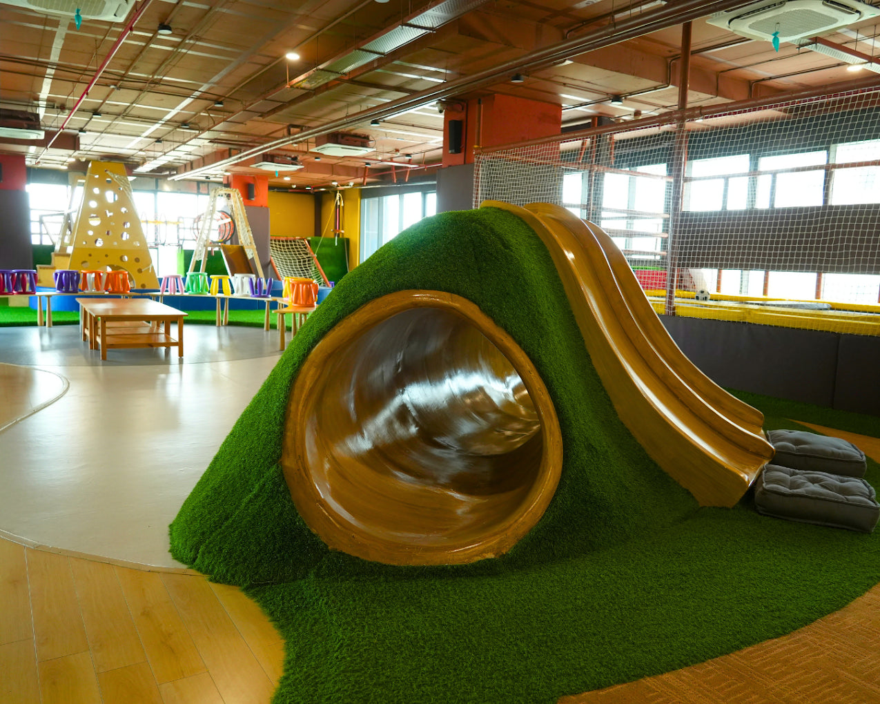 A colorful indoor playground with a large green tunnel slide and climbing structures for children.